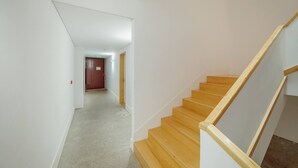 Un pasillo con escalera de madera, paredes blancas y suelo alfombrado.