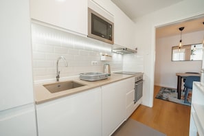 Een moderne keuken met witte kasten, een ingebouwde magnetron, een roestvrijstalen spoelbak en een compacte vaatwasser.