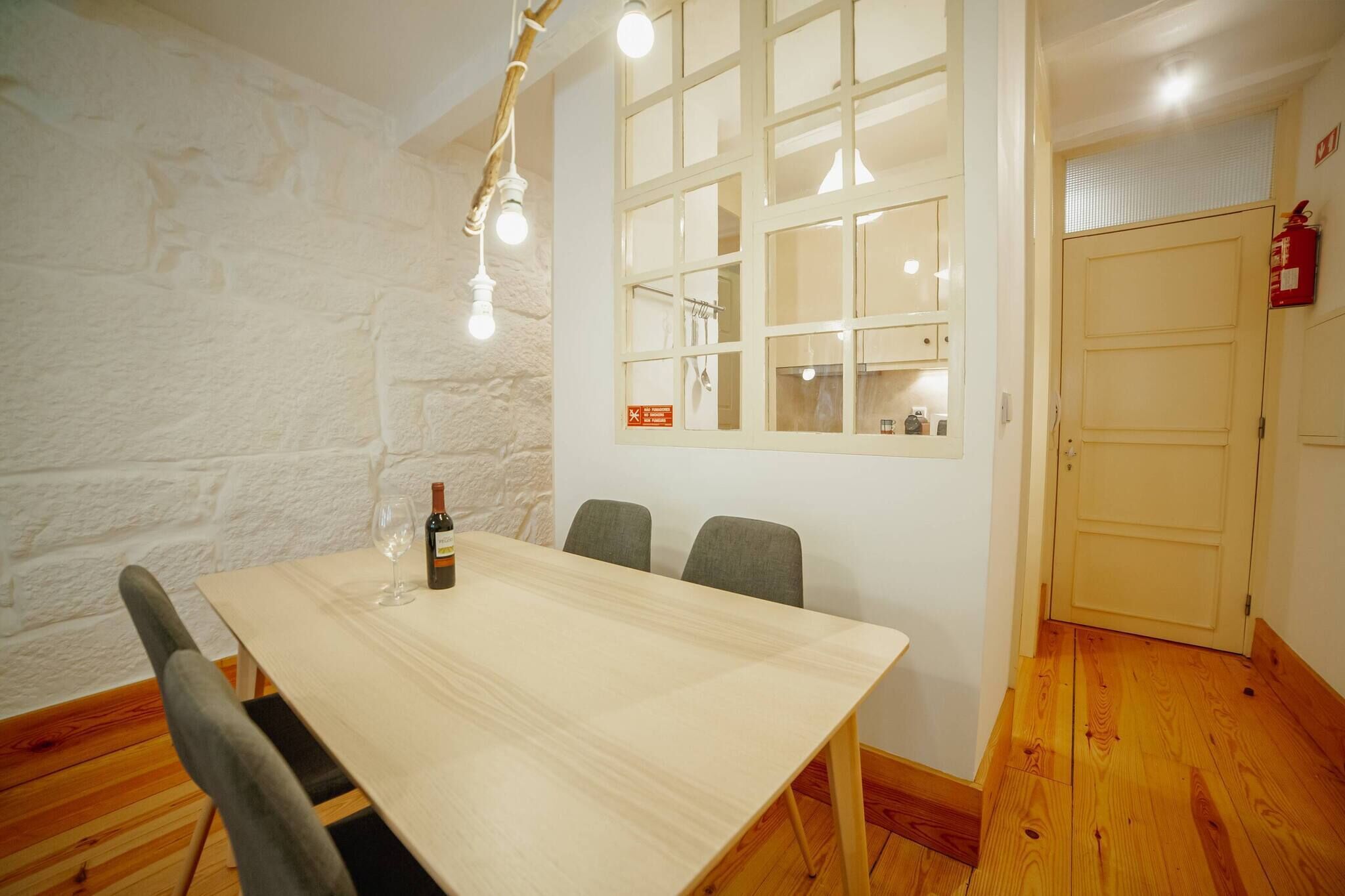 Una habitación con una mesa de madera, cuatro sillas, una botella de vino y una ventana con vistas a un edificio.
