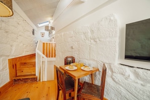 A rustic room with a wooden staircase, a dining table with plates of food, and a white textured wall.