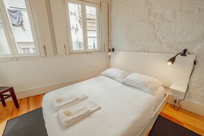 A neatly made bed with white linens and towels, a bedside lamp, and a window with curtains. - Charming Tiny House by Hosty (Porto)