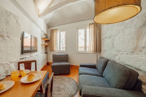A cozy living room with a wooden dining table, grey sofa, and a television on the wall.