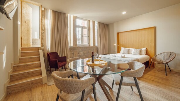 A hotel room with a bed, a round glass table with chairs, a staircase, and a view of the outside. - Flores Deluxe by Hosty (Porto)