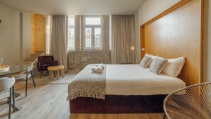 A hotel room with a large bed, a small round table, a chair, and a view of the city through large windows. - Flores Deluxe by Hosty (Porto)