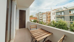 A balcony with a wooden table and chairs, a door, and a view of neighboring buildings. - Bonfim Vintage by Hosty (Porto)