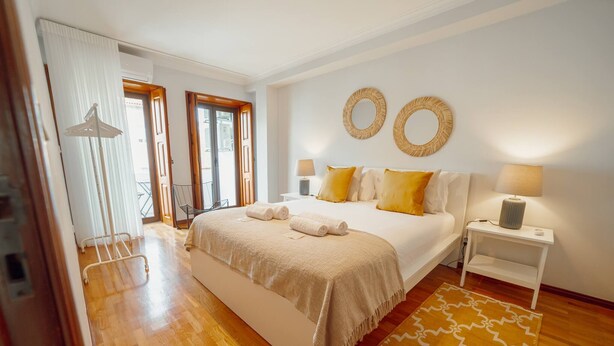 A bedroom with a large bed, two bedside tables, a window with curtains, and a wooden floor. - Bonfim Vintage by Hosty (Porto)