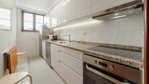 A modern kitchen with white cabinets, granite countertops, a built-in oven, and a window providing natural light. - Bonfim Vintage by Hosty (Porto)
