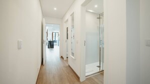 A modern hallway with a wooden floor, white walls, and a glass shower door.