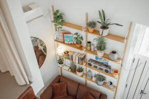 A living room with a brown sofa, wooden shelves with books and plants, a white radiator, and a white door. - Modern Studio by Hosty (Porto)