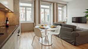 Een moderne keuken met een eethoek, een grijze bank en een aan de muur bevestigde televisie.