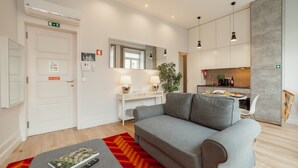 Een moderne woonkamer met een grijze bank, een wit bureau en een keuken in de achtergrond.