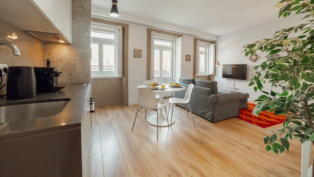 Een moderne keuken met een koffieapparaat, een eettafel met stoelen en een grijze bank.