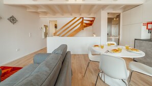 Een moderne leefruimte met een grijze bank, een witte eettafel met stoelen en een houten trap.
