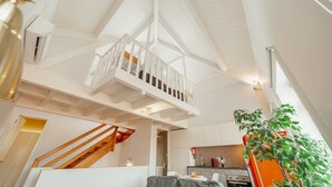 Een ruime living in loftstijl met een hoge nok, een houten trap en een keukenhoek.
