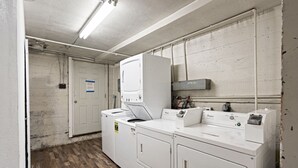 Een wasruimte met een witte deur, een wasmachine, een droger en een technische ruimte met een witte muur en een houten vloer.