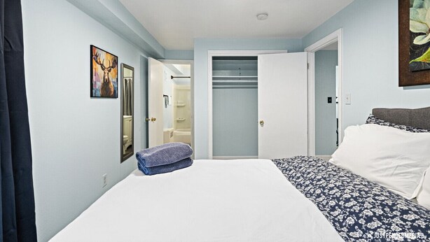 Een slaapkamer met een bed, een kledingkast, een badkamer zichtbaar door een geopende deur en een schilderij aan de muur.
