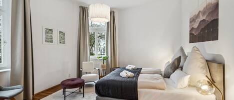 A modern bedroom with a bed, a desk, a chair, and a window with curtains.