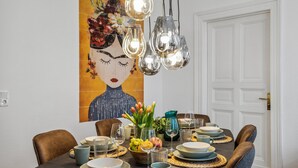 A dining area with a table set for four, featuring a modern chandelier, a large floral artwork on the wall, and a variety of tableware and glassware. - Old building apartment 2 bedrooms Augustaplatz Kurpark GOP Balitherme (Bad Oeynhausen)