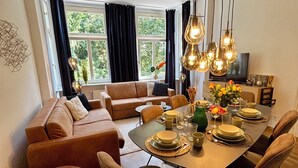 A modern living room with a sofa, dining table, and chairs. There is a TV and a plant on the table. - Old building apartment 2 bedrooms Augustaplatz Kurpark GOP Balitherme (Bad Oeynhausen)
