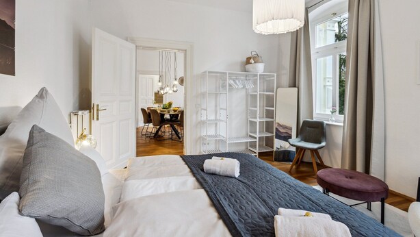 A modern bedroom with a large bed, a wardrobe, a dining area, and a view of the outdoors. - Old building apartment 2 bedrooms Augustaplatz Kurpark GOP Balitherme (Bad Oeynhausen)