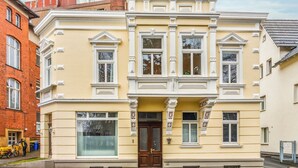 A two-story building with a yellow facade, large windows, and a central entrance with a dark wooden door. - Old building apartment 2 bedrooms Augustaplatz Kurpark GOP Balitherme (Bad Oeynhausen)