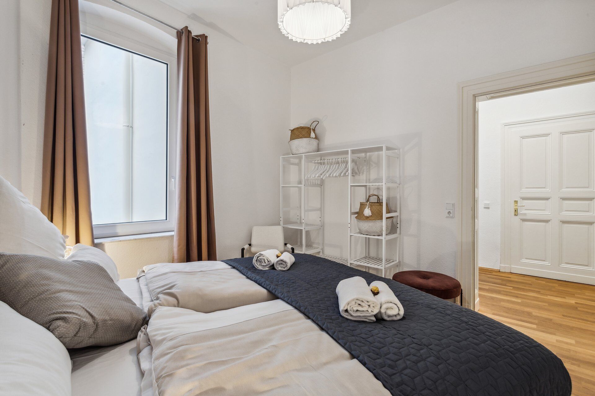 Ein ordentlich eingerichtetes Schlafzimmer mit einem Bett, einem Nachttisch, einem Kleiderschrank und einem Fenster mit Vorhängen.