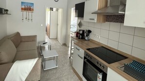 A modern kitchen with a built-in oven, a stove, and a microwave. There is a dining table with chairs and a sofa in the living area. - Panorama 180° (Unknown)