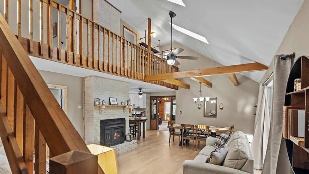 A spacious loft-style living area with a high ceiling, exposed wooden beams, a fireplace, a dining area, and a staircase leading to an upper level.