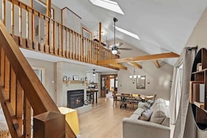 Un vaste espace de vie de style loft, doté d’un plafond haut, de poutres apparentes, d’une cheminée, d’un coin repas et d’un escalier menant à un niveau supérieur.