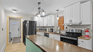 A kitchen with white cabinets, a stainless steel refrigerator, a microwave, a stove, and a wooden countertop.
