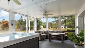 A covered outdoor area with a hot tub, seating, and large windows.