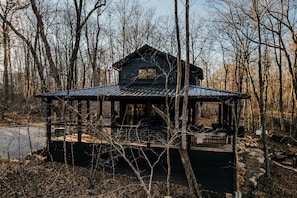 A cabin with a metal roof, surrounded by trees, and a dock extending into a body of water. - Sleepy Hollow at The Retreat at Sunset Bluff (Monteagle)