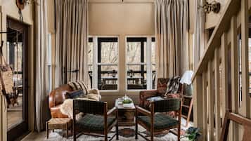 A cozy living room with a leather sofa, two armchairs, a coffee table, and a view of a wooden deck through large windows.