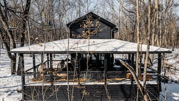 A wooden cabin with a covered porch and a snow-covered roof, surrounded by trees.