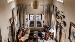 A cozy living room with a leather sofa, a patterned armchair, a coffee table, and a large window with curtains.