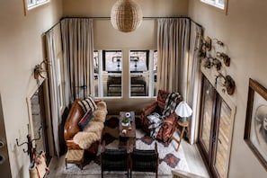 A cozy living room with a leather sofa, a patterned armchair, a coffee table, and a large window with curtains.