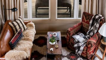A cozy living room with a brown leather sofa, a red patterned armchair, and a small wooden coffee table with a magazine and a plant.