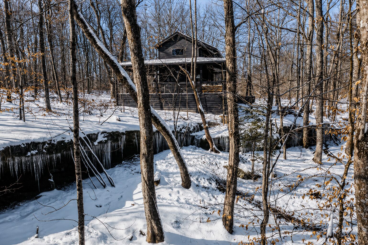 Eine Holzhütte, umgeben von schneebedeckten Bäumen und einem zugefrorenen Bach.