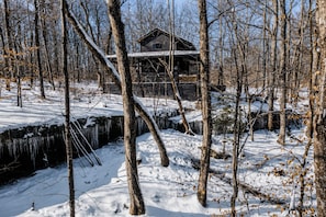 A cabin surrounded by snow-covered trees and a frozen stream. - Sleepy Hollow at The Retreat at Sunset Bluff (Monteagle)