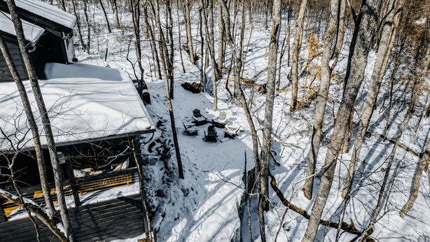 A cabin with a snow-covered roof, surrounded by a forest.