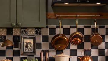 A kitchen with copper cookware hanging on the wall, a framed picture, and a variety of fresh vegetables on the counter.