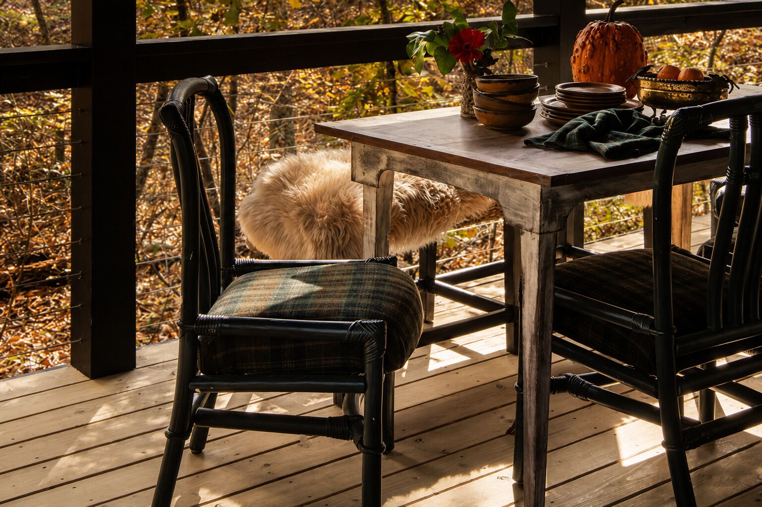 A wooden deck with a table and chairs, a fluffy white object, and a pumpkin.