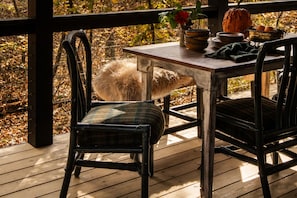 A wooden deck with a table and chairs, a fluffy white object, and a pumpkin.