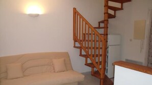 A living room with a beige sofa, a wooden staircase, and a white refrigerator. - T2 GOLFE DE LAVA BORD DE MER AVEC PISCINE (Appietto)