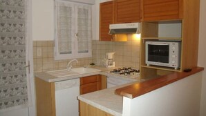 A compact kitchen with wooden cabinets, a gas stove, a microwave, and a dishwasher. - T2 GOLFE DE LAVA BORD DE MER AVEC PISCINE (Appietto)