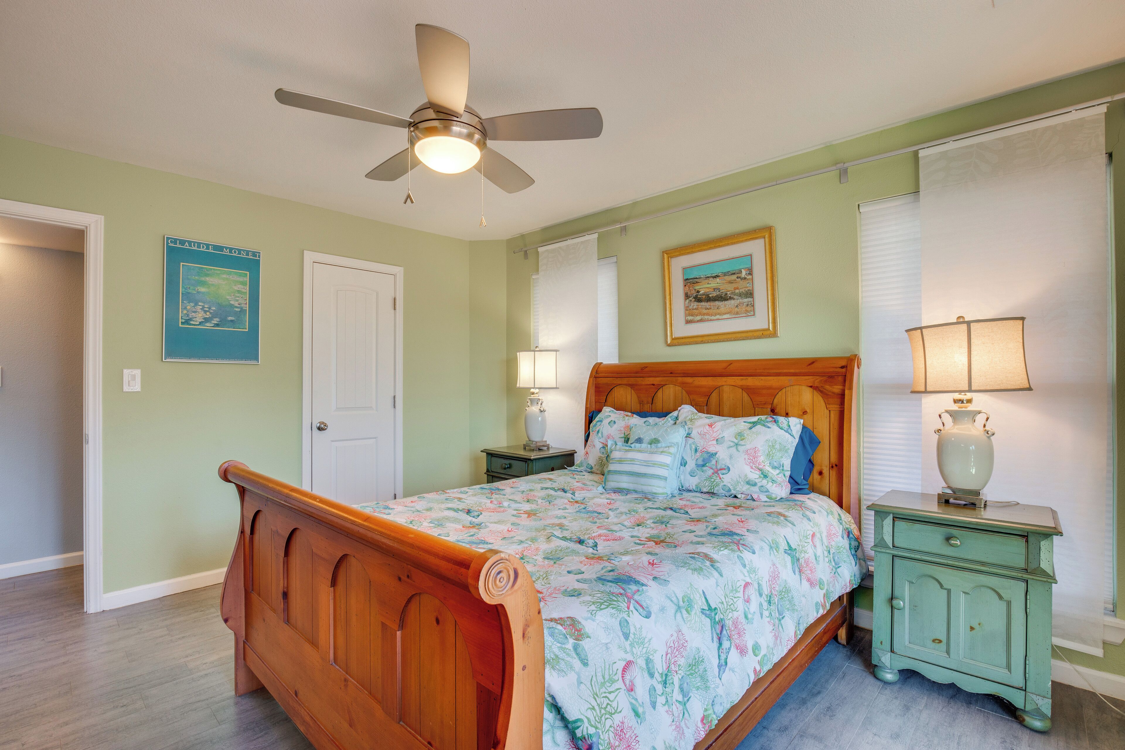 A bedroom with a wooden bed, a ceiling fan, two bedside tables with lamps, and a door.
