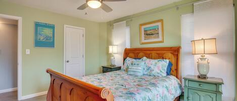 A bedroom with a wooden bed, a ceiling fan, two bedside tables with lamps, and a door.