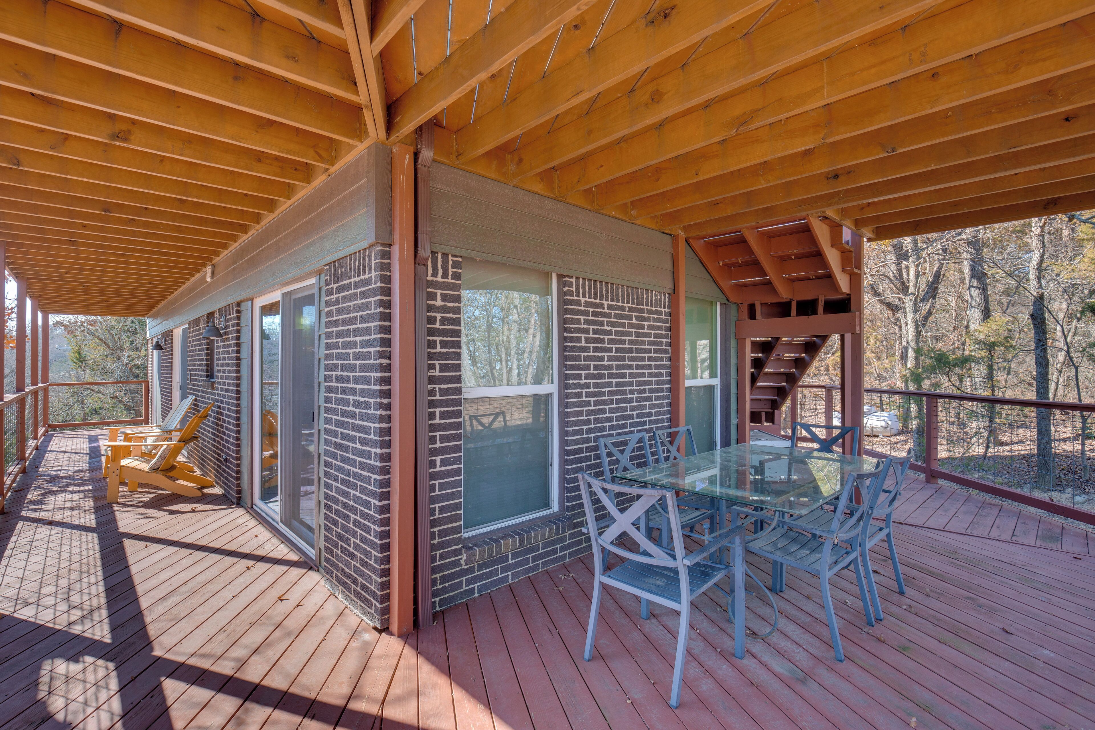 A covered deck with a glass table and chairs, a brick wall, and a wooden ceiling.