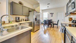 A modern kitchen with stainless steel appliances, a double sink, and a dining area with a table and chairs. - 11 Mi to Disney: Home w/ Pool in Davenport! (Davenport)