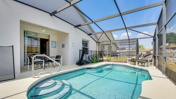 A swimming pool with a glass enclosure, lounge chairs, and a door leading to the building. - 11 Mi to Disney: Home w/ Pool in Davenport! (Davenport)